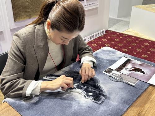 ■カーペット工業組合<br>「カーペットはすばらしい」をテーマに、壁・床面を目いっぱい使って、各社が新開発したデザイン・機能カーペットやサービスなどを出展。また、カーペットメンテナンス・クリーニングに関する相談コーナーを設けたほか、カーペット生産工程映像の放映や、Neo TAPIS(日本省力化機械㈱)によるハンドタフテッド製3Dタペストリーの、人手による丹念な仕上げ実演、さらに現在のカーペット産業のルーツに当たる、明治時代における「堺緞通」と藤本荘太郎及び村田伝七に関する展示も行われた。